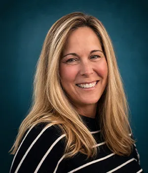 Smiling woman with long blonde hair in a black and white striped top, blue background.