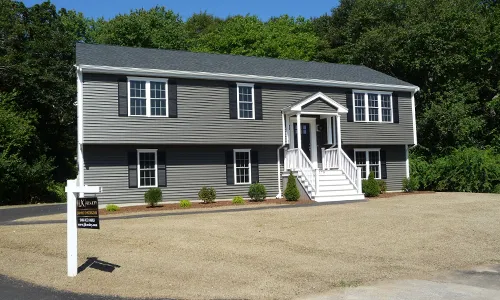 Gray two-story house with white trim, front steps, and a for sale sign in the yard.