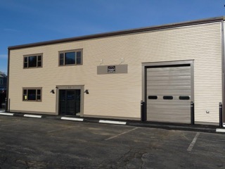 Tan industrial building with dark trim, windows, a double door, and a large garage door.
