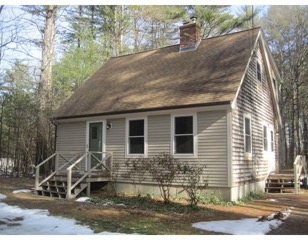 Small beige house with a steep roof, front steps, and light snow on the ground.