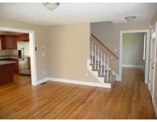 Open living space with hardwood floors, beige walls, kitchen, and staircase visible.