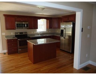 Modern kitchen with wooden floors, dark cabinets, stainless steel appliances, and an island.