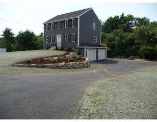 Two-story gray house with double garage, sloped driveway, and landscaped front yard.