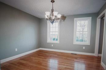 Empty dining room with hardwood floors, light gray walls, and two windows with a chandelier.