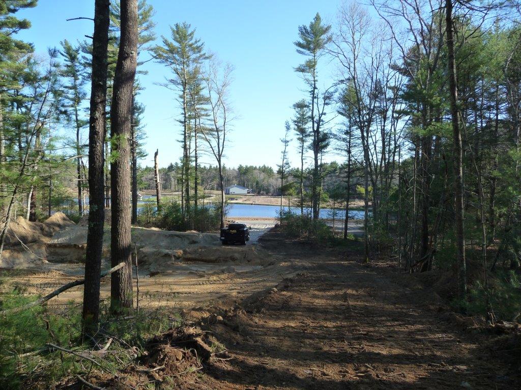 Dirt path through trees leading to a lake, with a small vehicle near the water.