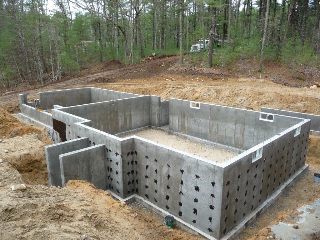 Concrete foundation walls for a new house under construction surrounded by dirt and trees.