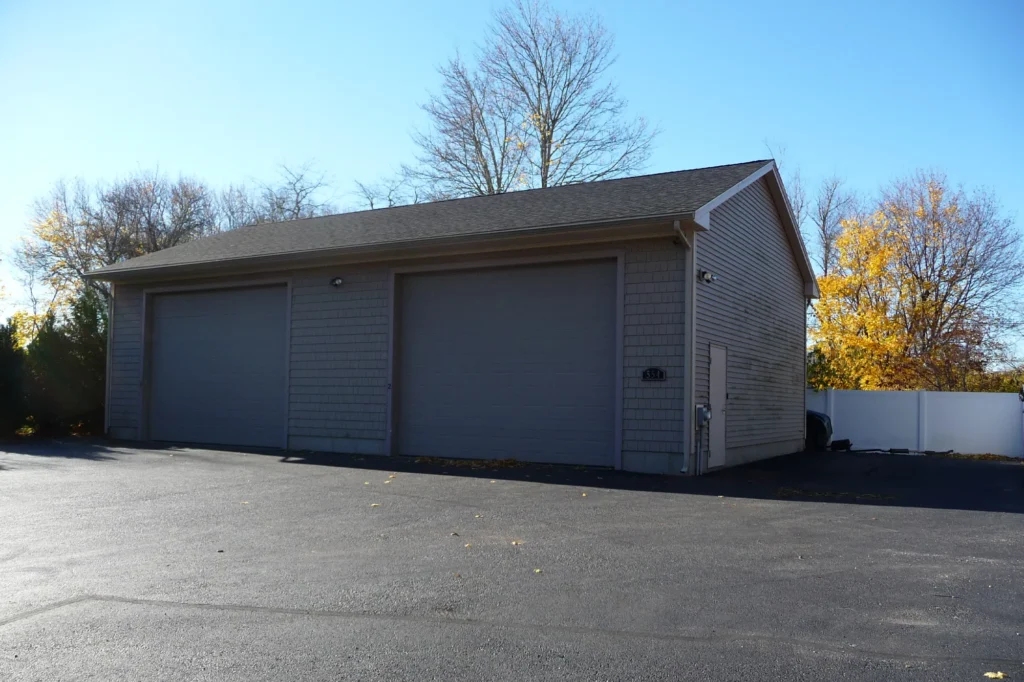 Gray three-car garage with closed doors on a paved driveway, trees in the background.