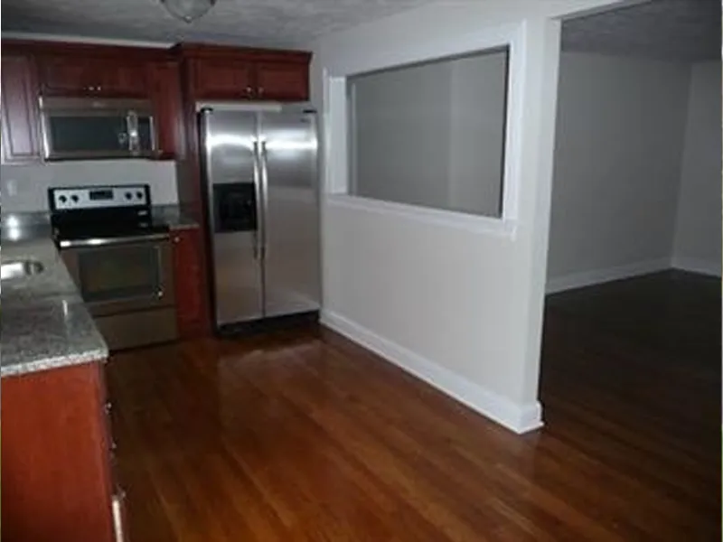 Kitchen with stainless steel appliances and hardwood floors, next to an empty room.