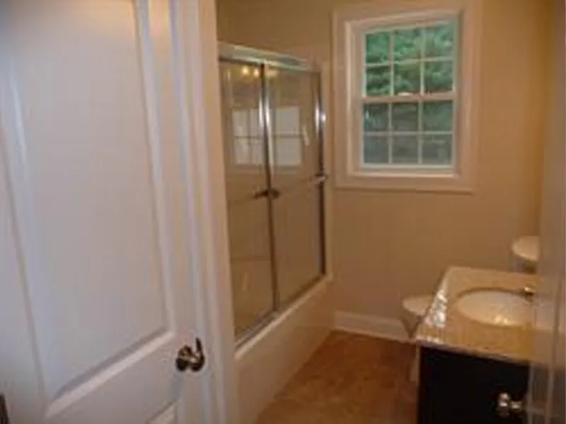 Small bathroom with a bathtub, glass shower doors, window, toilet, and sink.