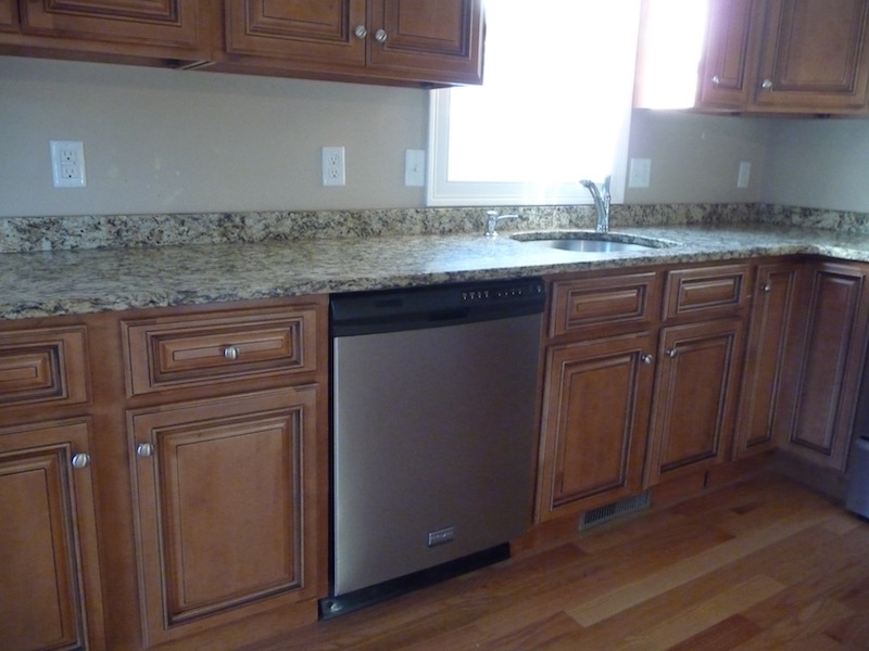Brown wooden kitchen cabinets, granite countertop, stainless steel dishwasher, and sink.
