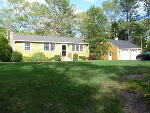 Single-story yellow house with attached garage, surrounded by trees and a large green lawn.