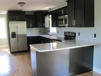 Modern kitchen with dark cabinets, stainless steel appliances, and light countertops.