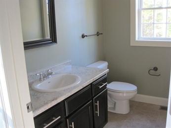Bathroom with a sink vanity, toilet, towel bar, and window letting in natural light.