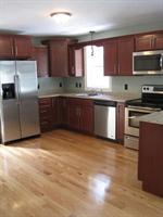 Modern kitchen with stainless steel appliances, wooden cabinets, and hardwood flooring.