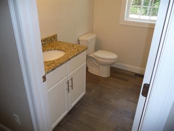 Small bathroom with a toilet, window, and vanity with granite countertop and white cabinets.