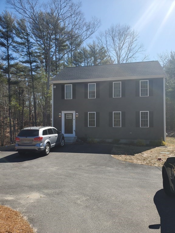 Gray two-story house with black shutters, two cars parked in driveway, trees in background.
