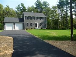 Two-story gray house with two garages, large lawn, and a blacktop driveway.
