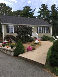 Single-story house with a front garden, flowers, and a curved sidewalk to the entrance.