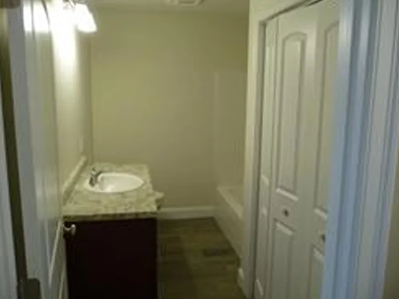 Narrow bathroom with a sink, granite countertop, tub, and white closet doors.