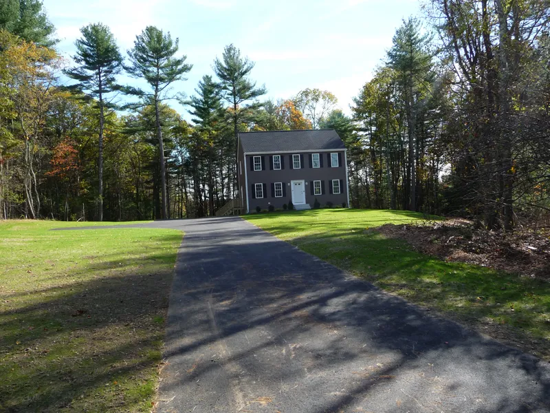 A two-story house with a long driveway, surrounded by trees and green grass.