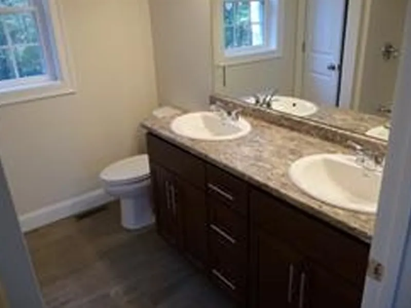 Bathroom with double sinks, brown cabinets, a toilet, and a window with natural light.
