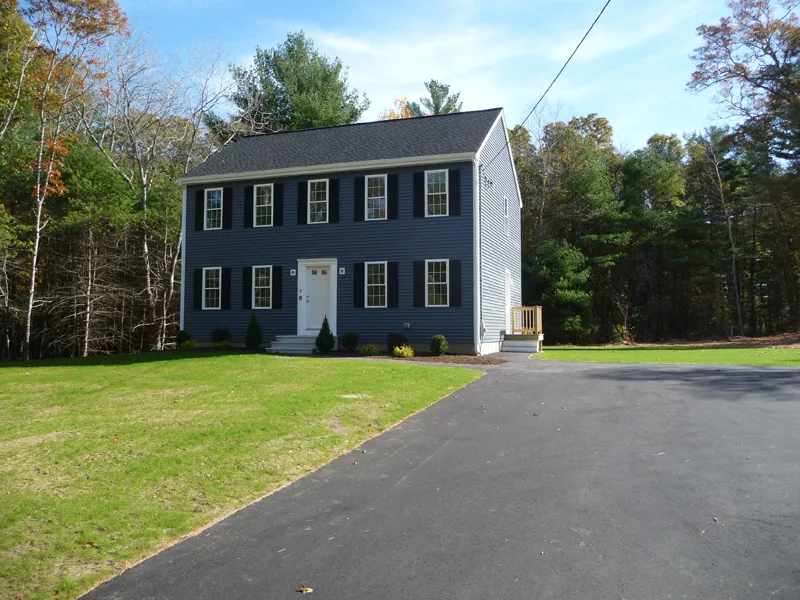 Two-story blue house with white trim, black shutters, and a large driveway in front.
