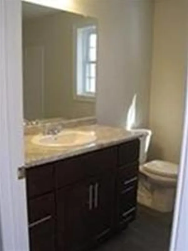Small bathroom with a dark wood vanity, sink, mirror, and a toilet by a window.