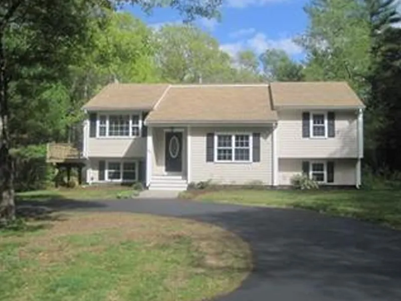 Two-story beige house with a gable roof and a curved driveway, surrounded by trees.