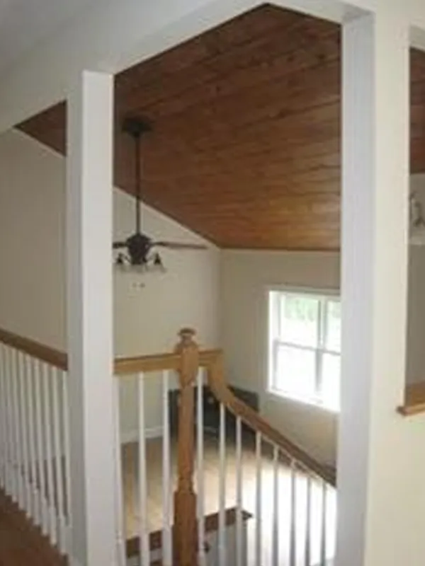 Staircase with wooden banister and ceiling, white walls, and a window letting in light.