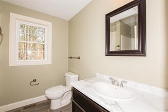 Bathroom with a white toilet, marble sink, wall mirror, and window letting in natural light.