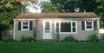 Single-story house with patriotic bunting and a flag, surrounded by green lawn and trees.