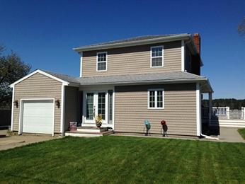 Two-story beige house with attached garage, white trim, and a green lawn under blue sky.