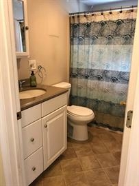 Small bathroom with white vanity, toilet, and blue-patterned shower curtain.