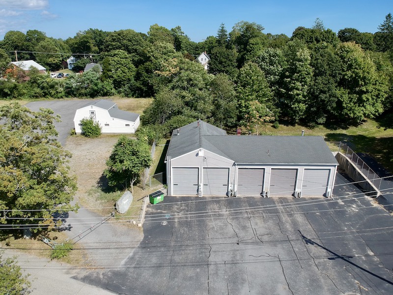 Aerial view of a four-bay garage and a small white building surrounded by trees.