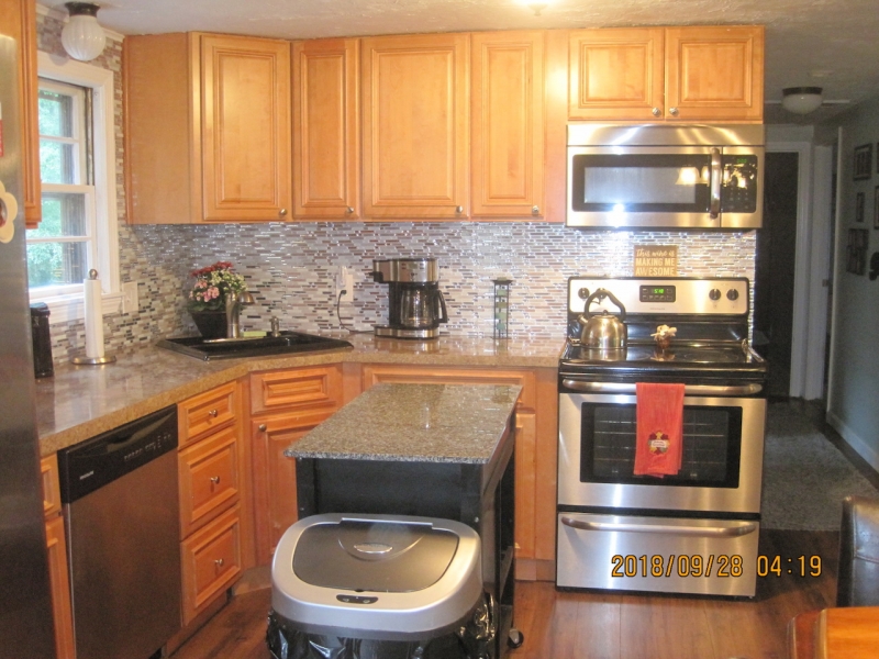 A kitchen with wood cabinets, stainless appliances, and a small island in the center.