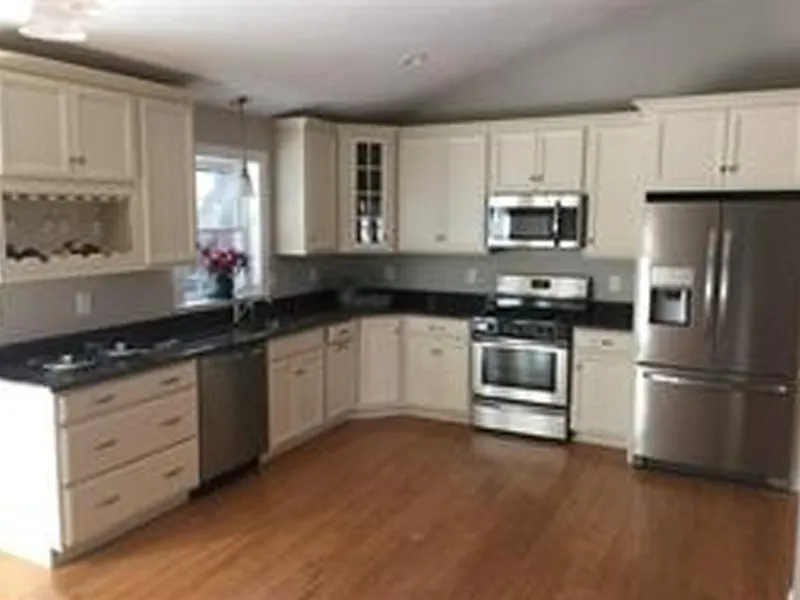Modern kitchen with white cabinets, stainless steel appliances, and hardwood floor.