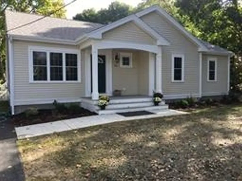 Single-story beige house with white trim, front porch, steps, and potted plants.