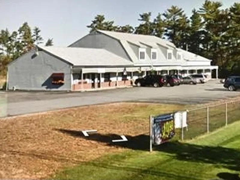 Gray two-story building with cars parked in front and a sign by a grassy area.