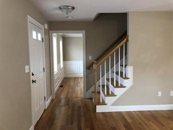 A hallway with wooden floors, white door, and a staircase with wooden railing.