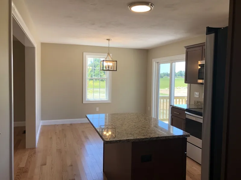 Bright kitchen with a granite island, wood floors, and large windows facing a green yard.