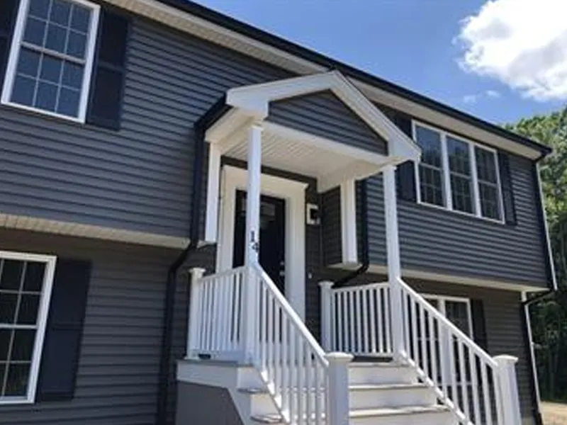 Two-story gray house with white trim, front porch, stairs, and a sunny blue sky.