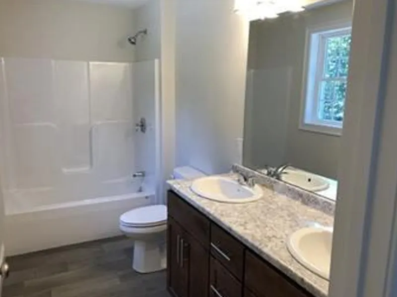 Modern bathroom with a double sink vanity, white bathtub, toilet, and a small window.
