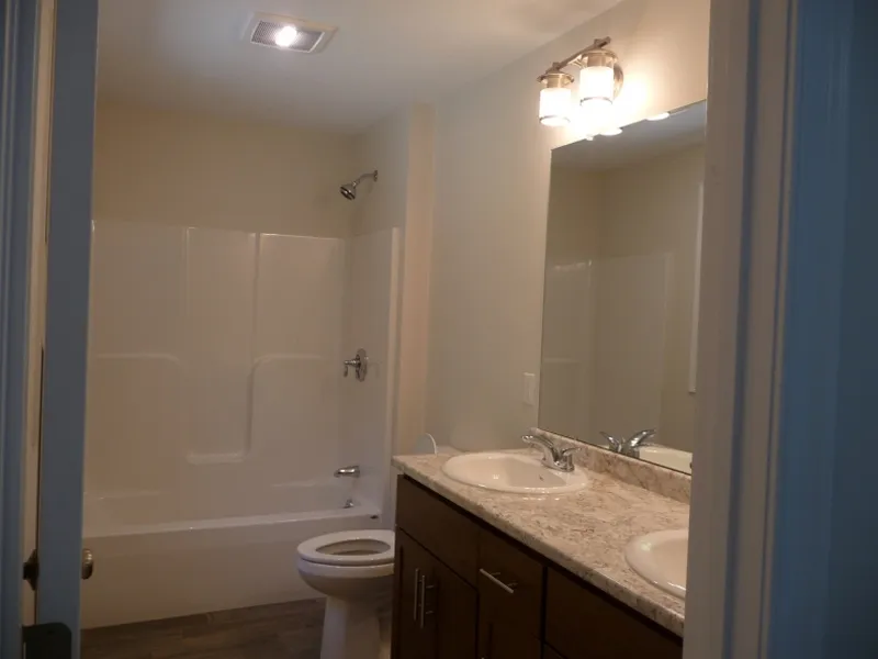 Bathroom with a bathtub, toilet, double sink vanity, mirror, and overhead lights.