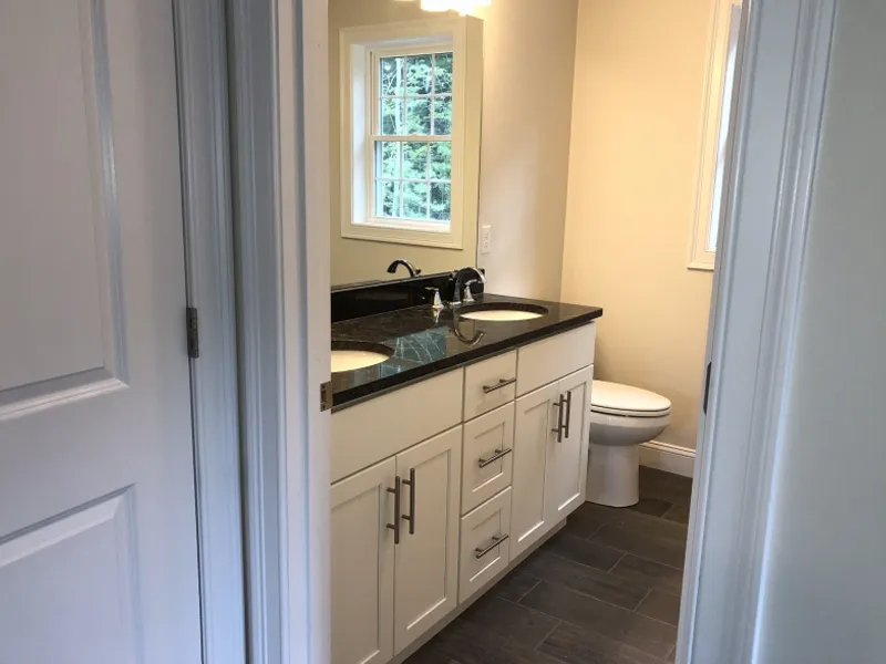 Modern bathroom with double sink vanity, black countertop, and a toilet by the window.