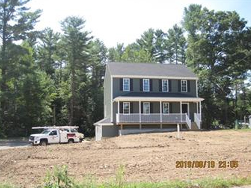 A green two-story house with a front porch and a white truck parked nearby.
