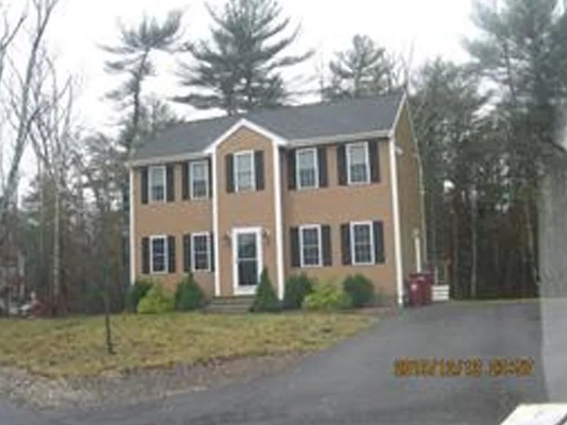 Two-story brown house with white trim, black shutters, and a driveway in front.