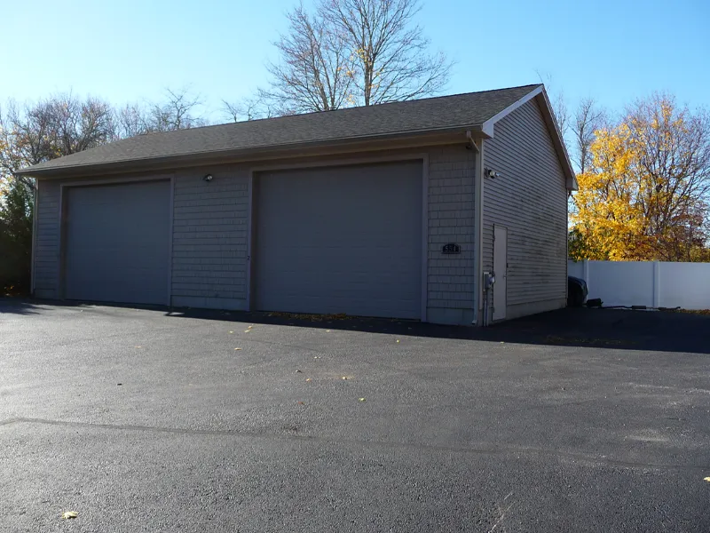 A large gray garage with three closed doors on a paved driveway in sunlight.