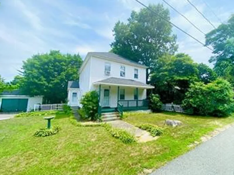 White two-story house with a front porch and green lawn on a sunny day.