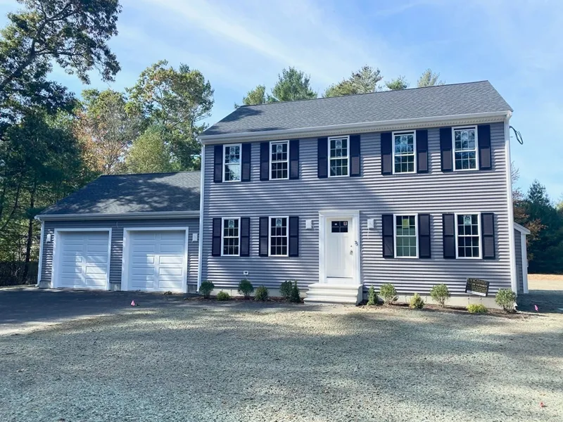 Two-story gray house with black shutters, double garage, and a gravel driveway.