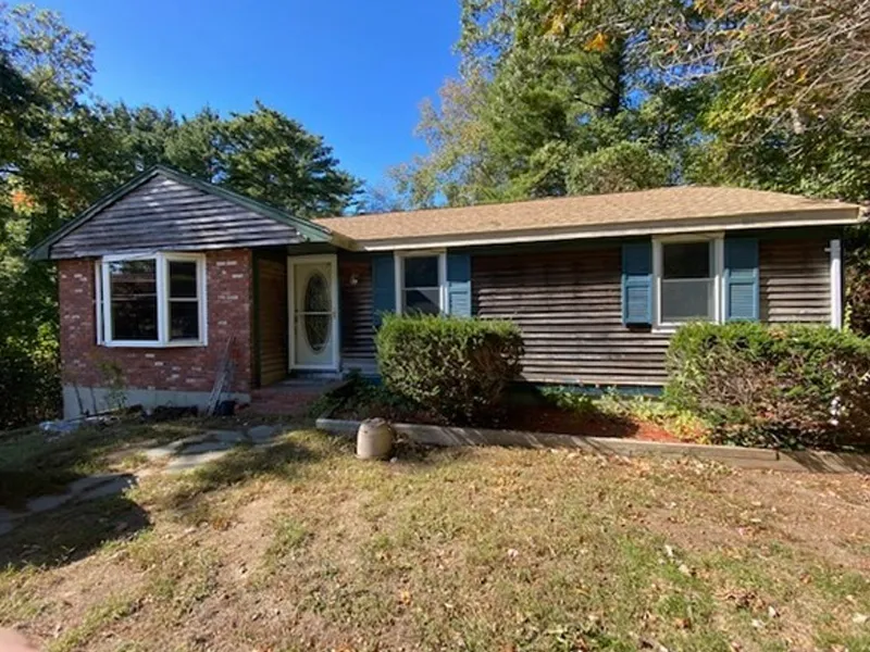 Single-story house with brick and wood siding, blue shutters, and shrubs in front yard.